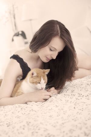 Beautiful young woman with cat in bedの写真素材