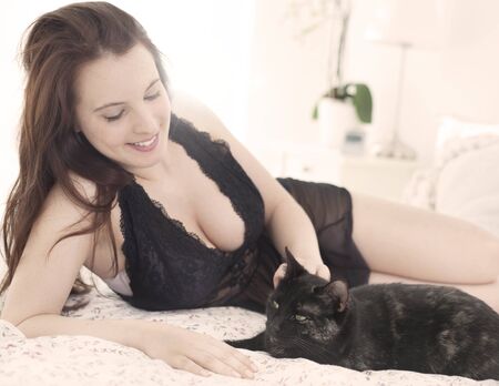Beautiful young woman with cat in bedの写真素材