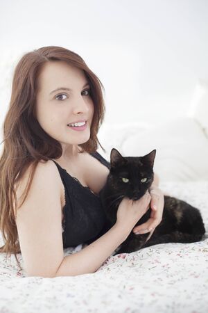 Beautiful young woman with cat in bedの写真素材