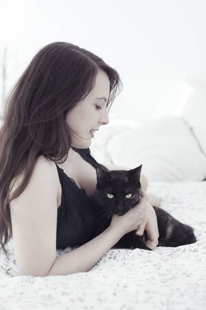Beautiful young woman with cat in bedの写真素材