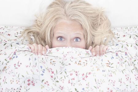 Blue eyes blond woman hiding behind blanket