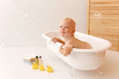 Bathing the baby in white bath with yellow rubber ducks, towels. Baby sitting in the bath and...
