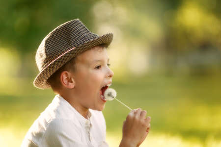 Portrait of a happy boy in the hat. Child is smiling in spring day. Kid is enjoying spring. Sunny day. Boy is jokes and eats dandelion. outdoor, close up.の写真素材