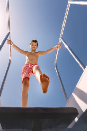 Young boy standing on a deck of yacht and going to go down in sunny day. Kid is wearing shorts, bottom view.の写真素材