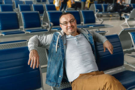 Traveler tourist man waiting to board into airplane, sitting in departure terminal in airport. Male passenger traveling by plane.の写真素材