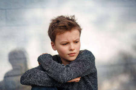 Sad boy is sitting next to the wall with furrowed brow. Kid is thoughtfulの写真素材