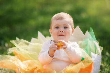 Pretty baby girl in egg shell at spring blooming meadow. Little girl smiling wearing yellow...