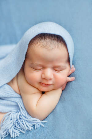 Sleeping newborn baby on a blue background covered by blanket. A few days from birth. Hands under the cheek.の写真素材