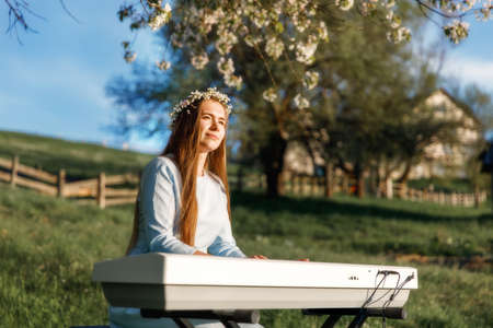 Girl playing a synthesizer piano in nature at sunset. A woman is 22 years old. An electric piano...