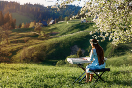 Girl playing a synthesizer piano in nature at sunset. A woman is 22 years old. An electric piano stands in a field in a village. Spring day in the countryside.の写真素材