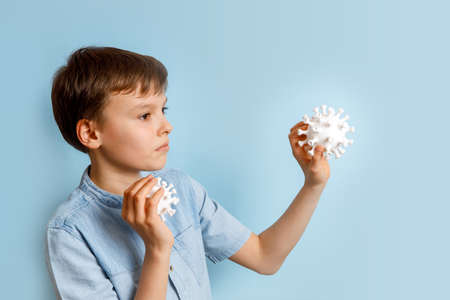 A boy against coronovirus on a blue background. Kid is looking at the virus. Hand is holding model Coronavirus . Coronovirus molecule printed model on a 3D printer.の写真素材