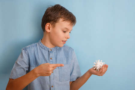 A boy in medicine mask against coronovirus on blue background. Kid is looking at the virus. Hand is holding model Coronavirus . Coronovirus molecule printed model on a 3D printer.の写真素材