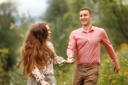 Happy loving couple are running together and holding hands, two people enjoying a walk through grass...