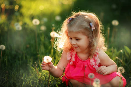 Portrait of happy blonde girl. Child is smiling in spring day. Kid is enjoying spring. Sunny day. Blonde girl is blowing dandelion. outdoor, close up.の写真素材