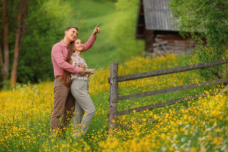 Young loving couple gently hugging on the wood house background, a lot of yellow flowers are around...