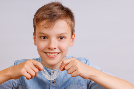 Positive child boy is holding mouth guards for his teeth and smiling. Banner. Invisible braces helps...