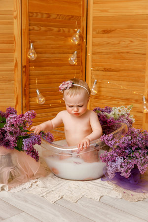 A baby, around one year old, is sitting in a transparent bathtub filled with milk. The child is playing in the water.の写真素材