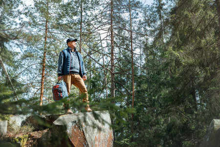 Smiling man with glasses and backpack hiking in a beautiful pine forest. Standing on mossy rocks, looking up. Outdoor adventure, positive emotion.の写真素材