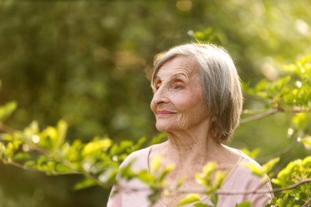 Elderly woman with gray hair looks off to the side as blurred leaves appear in the foreground,...
