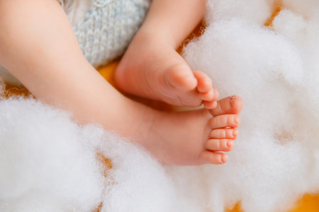 Close-up of a newborn baby feet and lower legs, partially covered in light blue knitted shorts,...