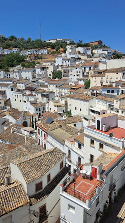 Close elevated view of a dense white old town with layered rooftops, terraces and narrow streets. Traditional tiled roofs and bright facades create geometric patterns under clear bの写真素材