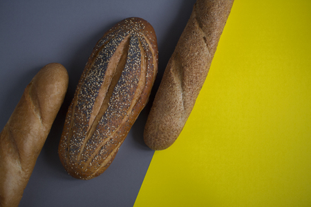 Bread and baguette on a yellow, gray background. View from above. Delicious loaf with poppy seeds and sesame. Home-made bread bakery products. Eco-friendly product. Healthy food. Place for text.の写真素材