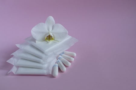 Feminine hygiene during menstruation. Menstrual cycle. Hygiene products for women. Pads and tampons with an orchid flower on a pink background. Gentle body care. Place for text.の写真素材