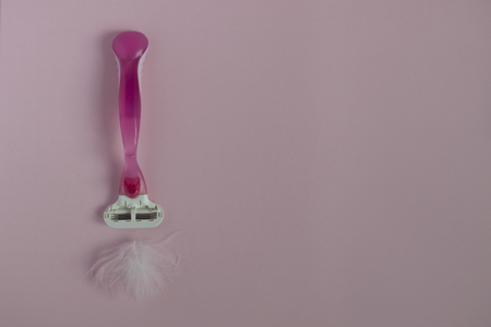 Care for the female body. Removal of unwanted body hair. Razor with a feather on a pink background. Hygiene and gentle care. Place for text.の写真素材