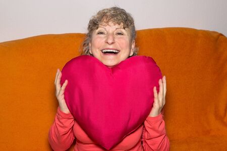 Pensioner smiling while holding a red heart in her handsの写真素材