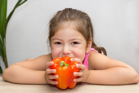 A little girl holds a pepper with both hands to her mouthの写真素材