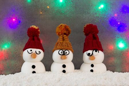Three snowmen with knit caps sitting in the snow in front of a colorful backgroundの写真素材