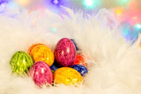 Many colorful eggs in a nest of white feathers