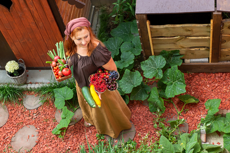 Young peasant woman in the garden carries bowls with fruits and vegetablesの写真素材