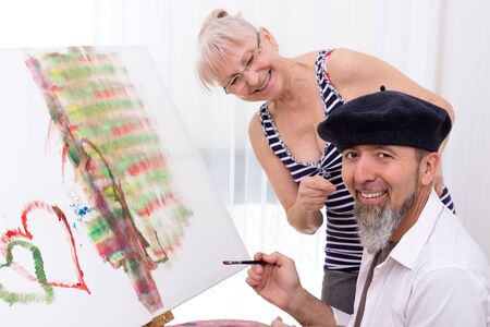Man in beret sits in front of an easel and smiles at the cameraの写真素材