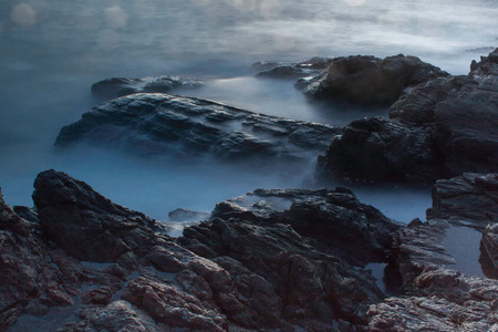 Ocean waves crashing onto the rocks in the sunsetの写真素材