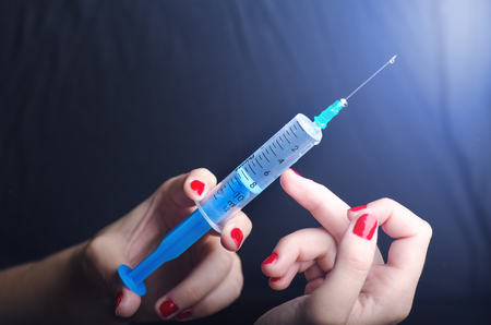 Medical injection on dark background. Medicine plastic vaccination equipment with needle. Health and care. Vaccination. Medicine background. Studio isolated. Phobia, Woman hand keep a injectionの写真素材