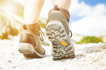 Woman hiker walk on a rocky ground. Sunny day.Trekking boots.Lens flare. Succesful backpacker. Stone. Stepの写真素材