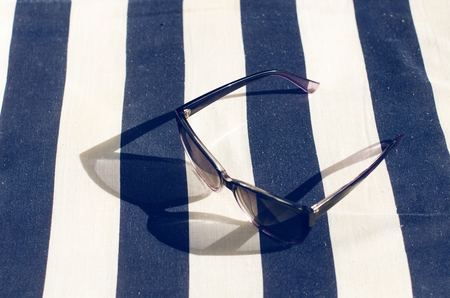 Black mirrored sunglasses on a blanket. Shadow from glasses. Sunlight. Summer conceptの写真素材