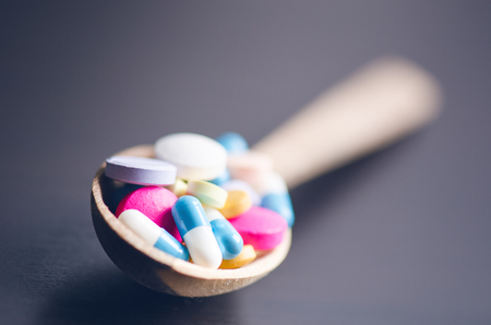 Full wooden spoon of pills. Pharmacy background on a black table. Tablets on a black background. Pills. Medicine and healthy. Close up of capsules. Differend kind of pillsの写真素材