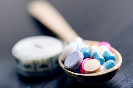 Pharmacy background on a black table with measuring tape. Tablets on a wooden spoon. Pills. Medicine and healthy. Close up of capsules. Differend kind of pillsの写真素材
