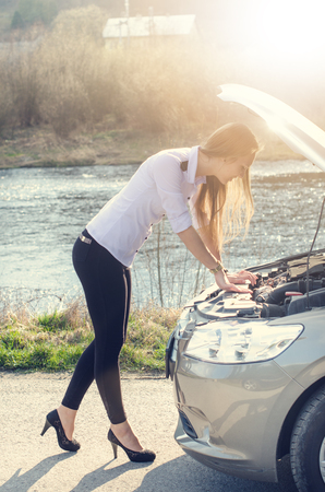 Woman crouching on the road next to a red warning triangle. Sad person. Damaged car. Natural background. Car accident.の写真素材