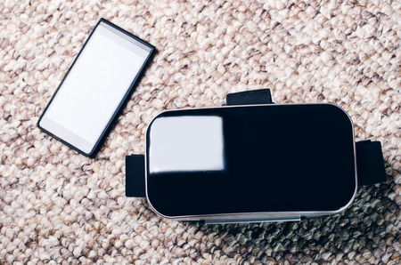 Virtual reality goggles lie on a carpet with mobile phone. Technology background.