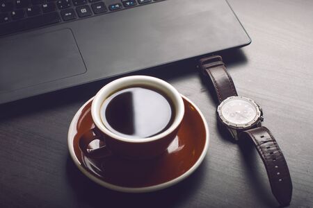 Cup of coffee on a dark table. Concept of business. Laptop, coffee, watch.