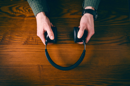 Man hand keep headphones on a wooden table with accessory such as phone, glasses. Concept of music.の写真素材