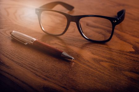 Glasses and pen on a wooden natural table. Office. Concept of work in a office and accessories.の写真素材