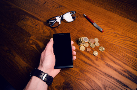 Man hand holding a phone. Concept of technology and business. Glasses, money, and pen on a table. Office background.の写真素材