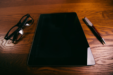 Cellphone, tablet, laptop with glasses and pen. Natural wooden table. Office background. Concept of technologyの写真素材