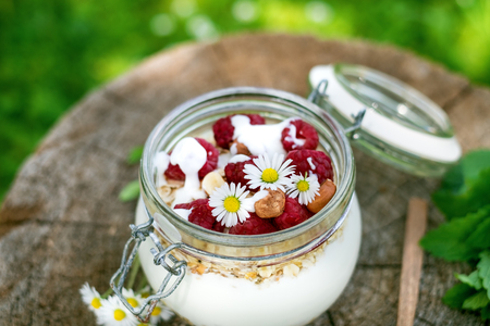 Full jar of muesli, yogurt, raspberries, nuts on a wood in a garden. Homemade breakfast cereals food. Healthy eating.の写真素材