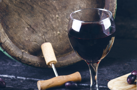 Glass and bottle of wine on a wooden barrel. Burnt, black wooden background. Vintage. Copyspace for a text. Grapes and green vine.の写真素材