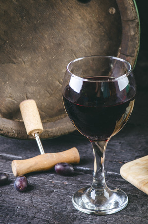 Glass and bottle of wine on a wooden barrel. Burnt, black wooden background. Vintage. Copyspace for a text. Grapes and green vine.の写真素材